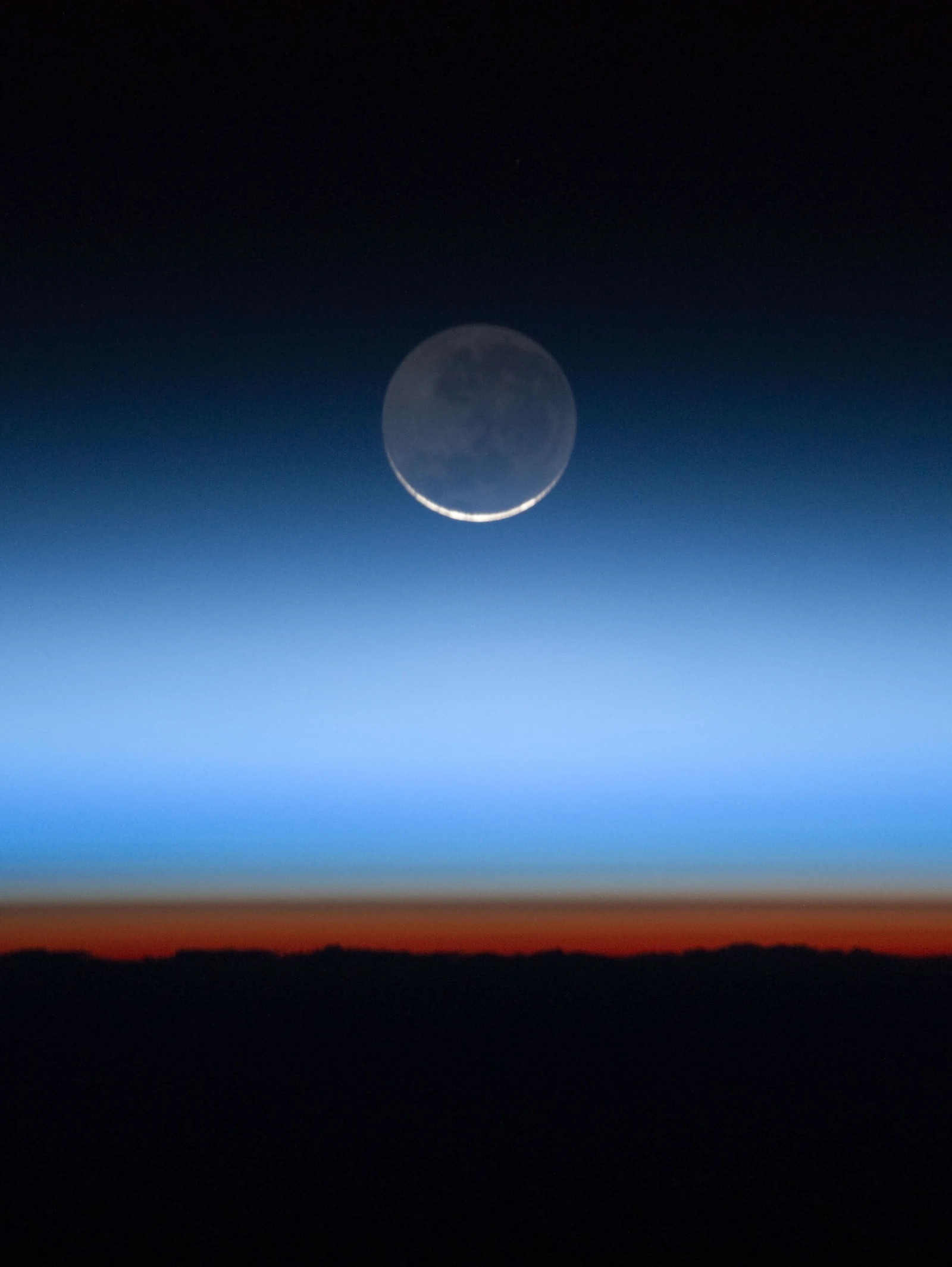 The Moon seen through the blue layers of Earth's atmosphere, above the orange troposphere and the night side of Earth, photographed from the International Space Station
